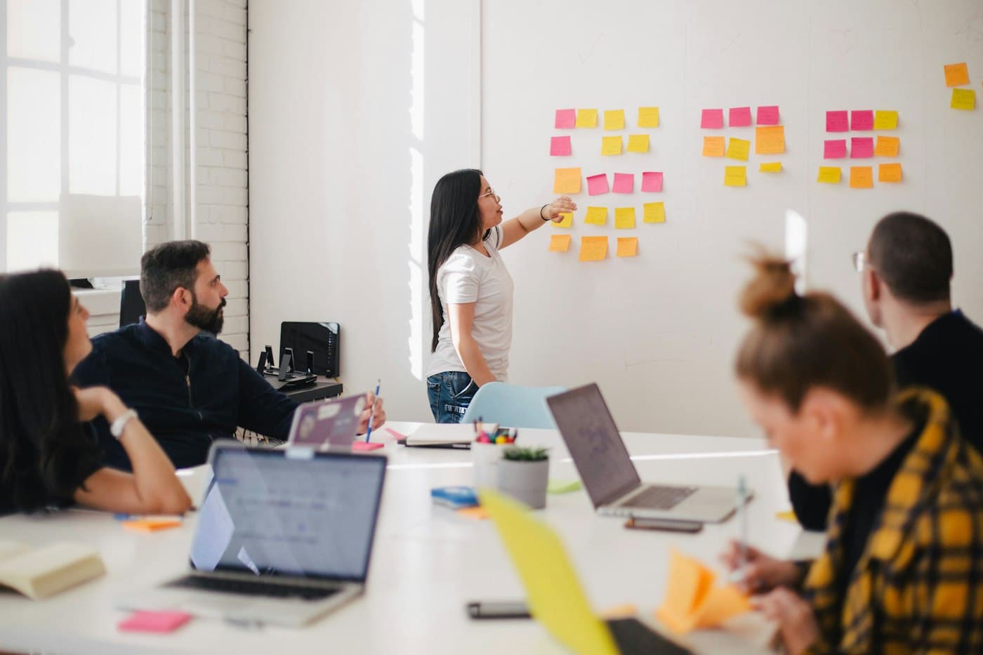 Team in een lichte vergaderruimte; een collega ordent post-its op de muur